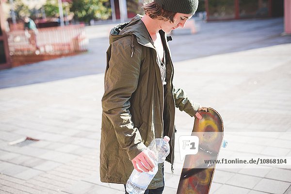 Junge männliche Skateboarderin  die eine Flasche Wasser hält.
