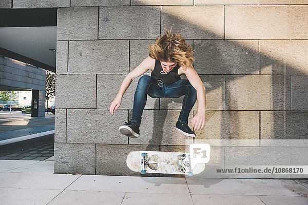 Junger männlicher Skateboarder beim Skateboarden Sprungtrick über Skateboard