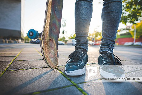 Beine und Füße eines jungen männlichen Skateboardfahrers  der auf dem Bürgersteig steht.