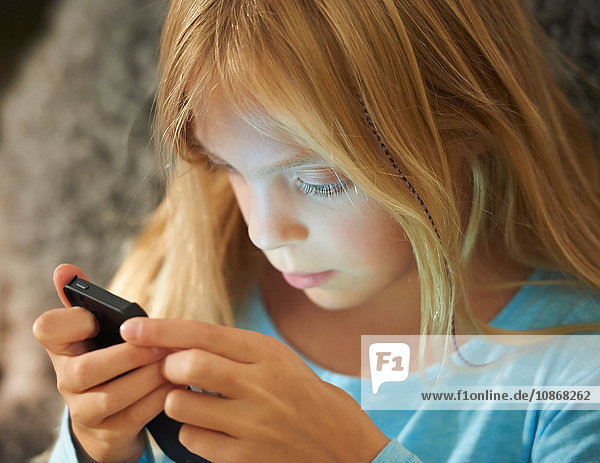 Junges Mädchen schaut auf ein Smartphone  das Gesicht wird vom Schein des Bildschirms beleuchtet