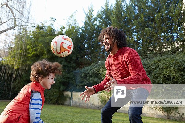 Vater und Sohn spielen lächelnd mit Fussball im Garten