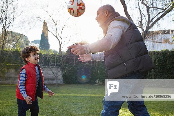 Grossvater und Enkel spielen lächelnd mit Fussball