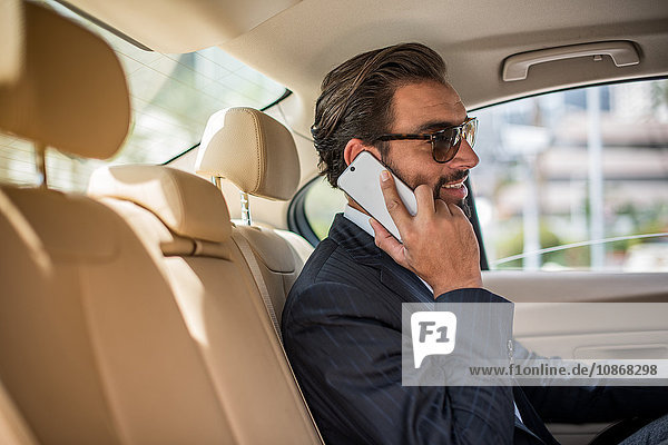 Junger Geschäftsmann auf dem Rücksitz eines Autos  der eine Sonnenbrille trägt und mit einem Smartphone spricht  Dubai  Vereinigte Arabische Emirate