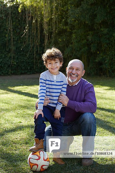 Grossvater und Enkel mit Fussball schauen lächelnd in die Kamera
