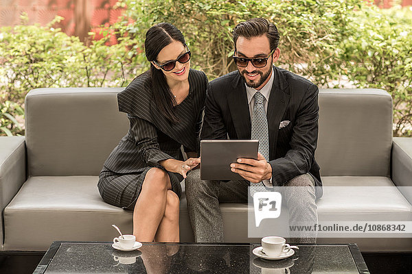 Geschäftsmann und -frau lesen digitales Tablet auf Hotelgartensofa  Dubai  Vereinigte Arabische Emirate