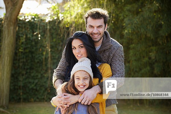 Parents standing behind daughter  arms around  looking at camera smiling