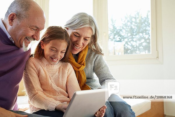 Großeltern am Fenstersitz mit digitalem Tablett  die Enkelin schaut lächelnd nach unten