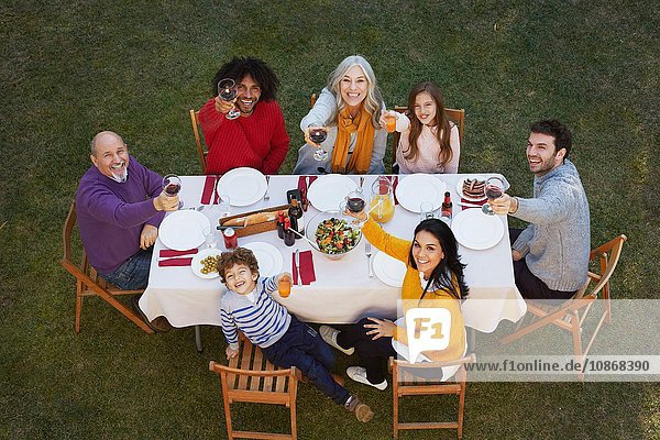 Draufsicht auf eine Mehrgenerationen-Familie  die im Freien speist  in die Kamera schaut und lächelnd anstößt