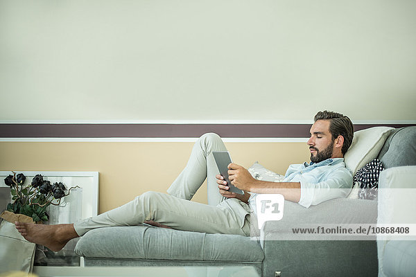 Junger Mann auf Hotelzimmer-Chaiselongue mit digitalem Tablett liegend  Dubai  Vereinigte Arabische Emirate