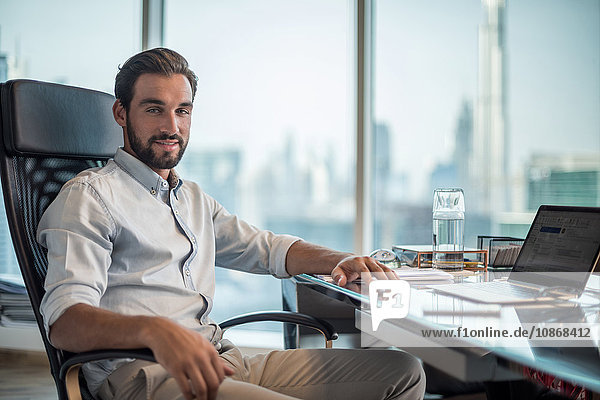Porträt eines Geschäftsmannes am Schreibtisch mit Fensteransicht des Burj Khalifa  Dubai  Vereinigte Arabische Emirate