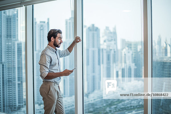 Businessman with smartphone staring through window with skyscraper view  Dubai  United Arab Emirates