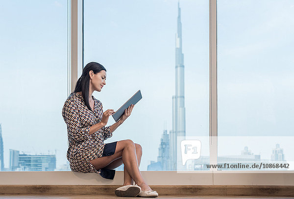 Geschäftsfrau mit digitalem Tablet am Fenster sitzend  Dubai  Vereinigte Arabische Emirate
