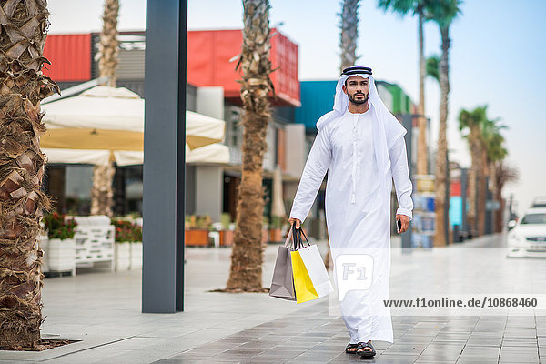 Mann in traditioneller Kleidung aus dem Nahen Osten geht mit Einkaufstaschen durch die Straße  Dubai  Vereinigte Arabische Emirate