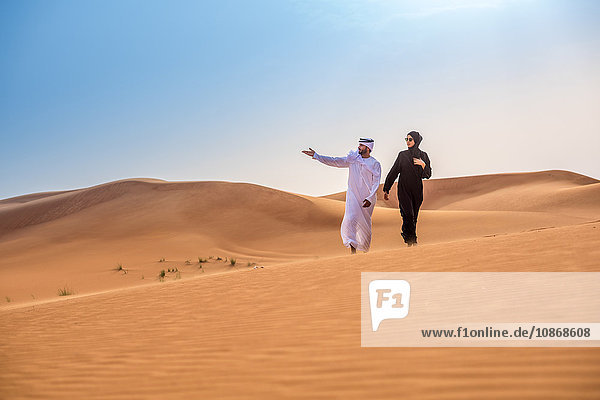Paar in traditioneller nahöstlicher Kleidung  die von einer Wüstendüne aus zeigt  Dubai  Vereinigte Arabische Emirate