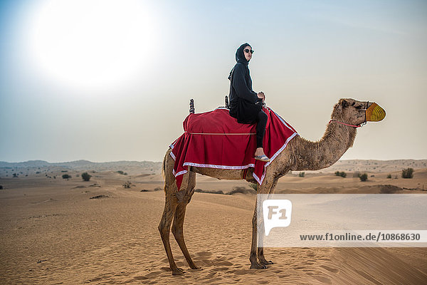 Junge Frau in traditioneller nahöstlicher Kleidung auf Kamel in der Wüste  Dubai  Vereinigte Arabische Emirate