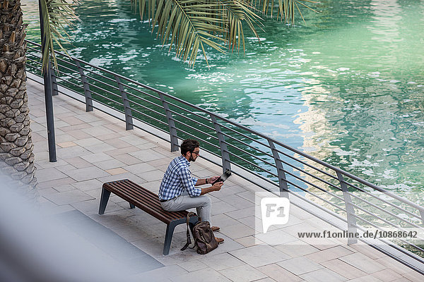 Hochwinkelansicht eines jungen Mannes der am Wasser sitzt mit einem digitalen Tablet Dubai Vereinigte Arabische Emirate