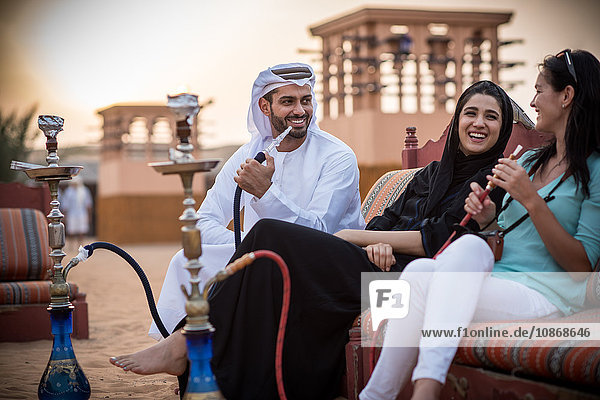 Einheimisches Paar in traditioneller Kleidung raucht Shisha auf dem Sofa mit einer Touristin  Dubai  Vereinigte Arabische Emirate