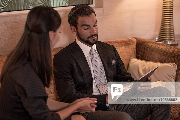 Geschäftsmann und -frau sitzen auf Hotelsofa und schauen auf digitales Tablet