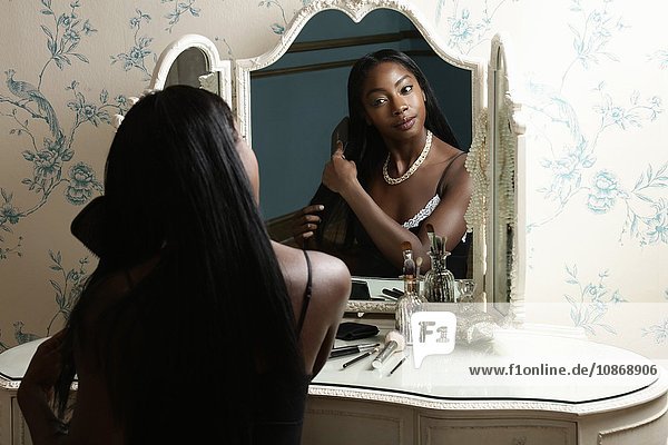 Junge Frau sitzt am Schminktisch  schaut in den Spiegel und bürstet sich die Haare
