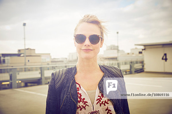 Porträt einer mittel-erwachsenen Frau mit Sonnenbrille auf einem Parkplatz auf dem Dach