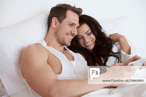Junges Paar sitzt im Bett und stöbert auf einem digitalen Tablet