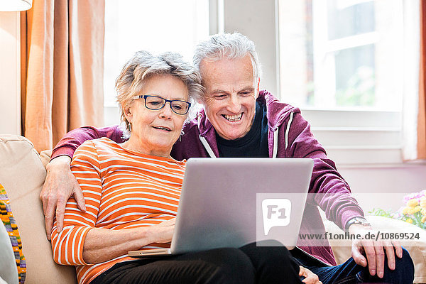 Älteres Ehepaar auf Wohnzimmer-Sofa mit Blick auf Laptop