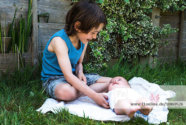Boy tickling baby brother in garden