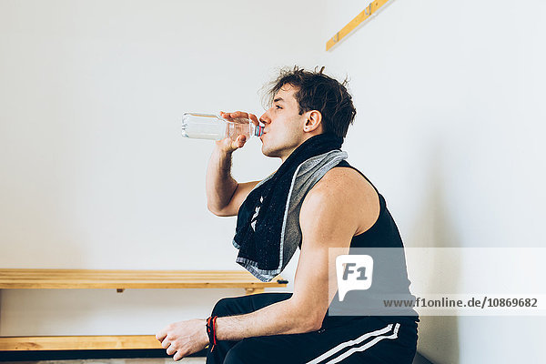 Man sitting in changing room drinking water from plastic bottle
