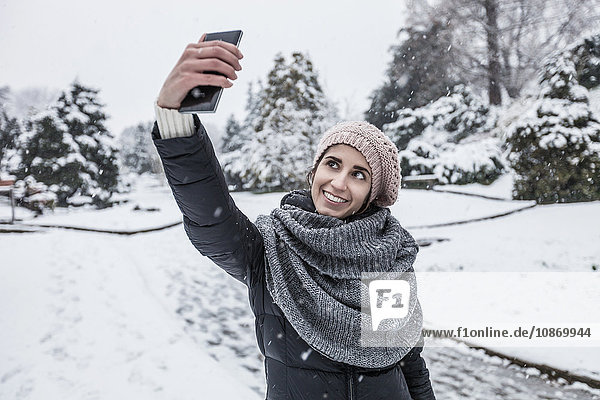 Woman on snow covered landscape using smartphone to take selfie
