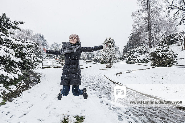 Frau auf schneebedeckter Landschaft springt mit offenen Armen in die Luft