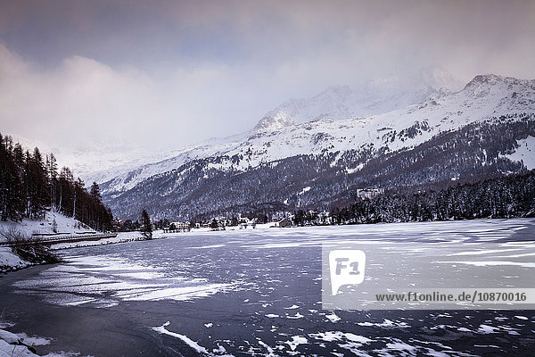 Gefrorener See und Dorf unter einem schneebedeckten Berg  Engadin  Schweiz