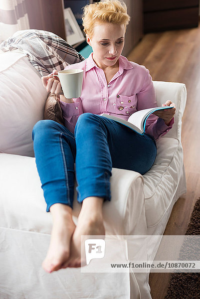 Woman reading and having coffee on sofa