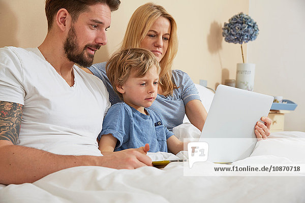 Mutter und Vater mit Sohn mit digitalem Tablett im Bett