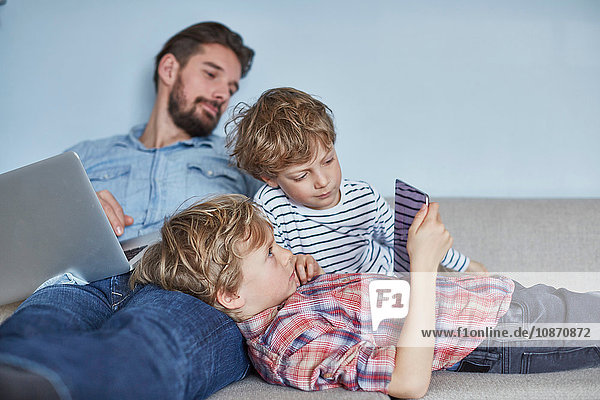 Boys lying on sofa with father using technology