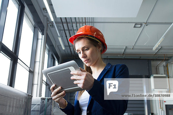 Woman in warehouse wearing hard hat looking at digital tablet