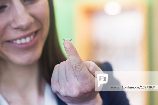 Woman holding contact lens on finger smiling