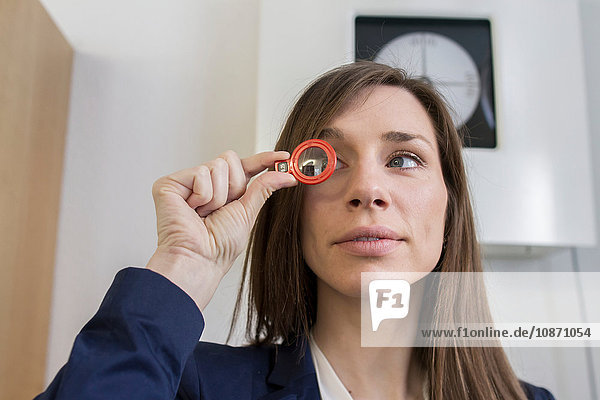 Frau im Büro eines Optikers schaut durch ein optisches Werkzeug