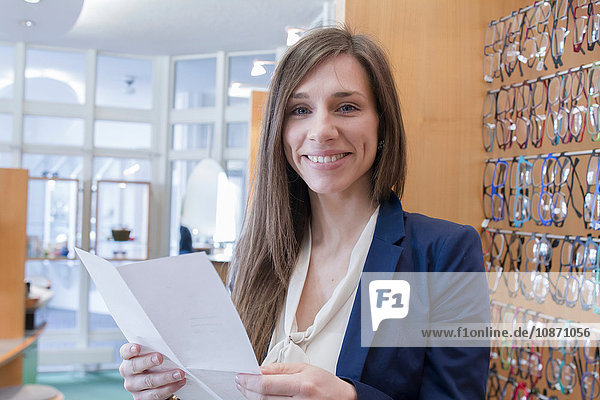 Sales assistant in opticians holding paperwork looking at camera smiling