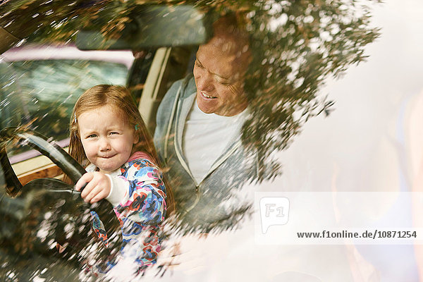 Blick durch die Windschutzscheibe einer Tochter  die auf dem Schoß des Vaters sitzt und Auto fährt