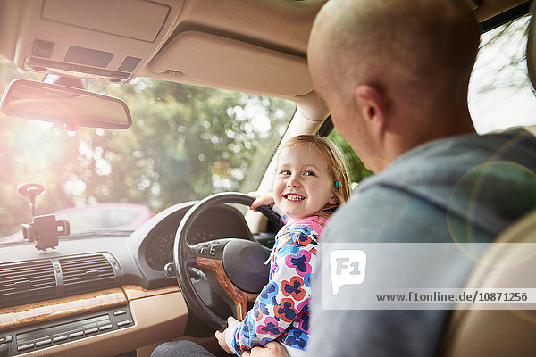 Über-Schulter-Ansicht einer Tochter  die auf dem Schoß des Vaters sitzt und Auto fährt