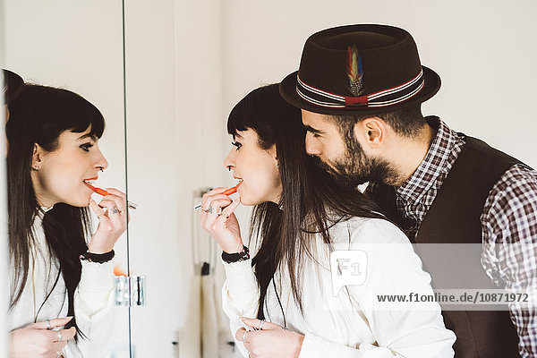 Young man with woman applying lipstick in front of mirror