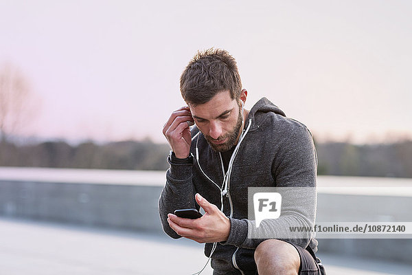Mittelgroßer erwachsener Mann  im Freien  Smartphone anschauend  Kopfhörer tragend