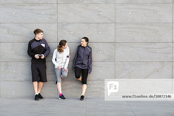 Three friends  wearing sports clothing  leaning against wall  chatting