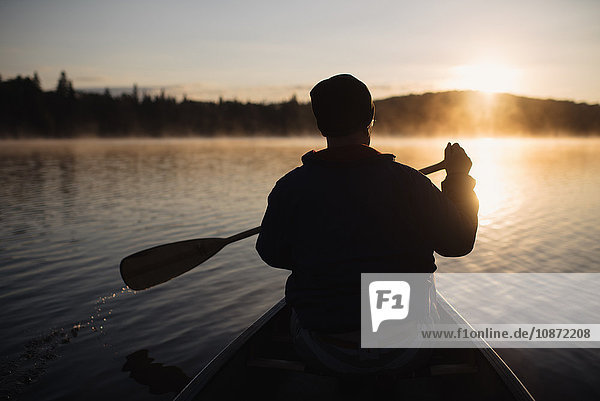 Senior man canoeing on lake at sunset rear view