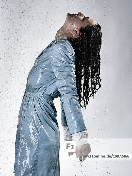 Seitenansicht einer Frau  die einen wasserdurchtränkten Regenmantel trägt und den Kopf zurückwirft