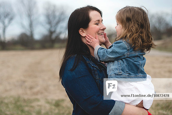 Mutter hält junge Tochter  im Freien  von Angesicht zu Angesicht  lächelnd