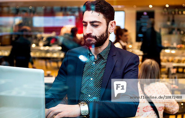 Geschäftsmann sitzt am Fenster eines Cafés und tippt am Laptop