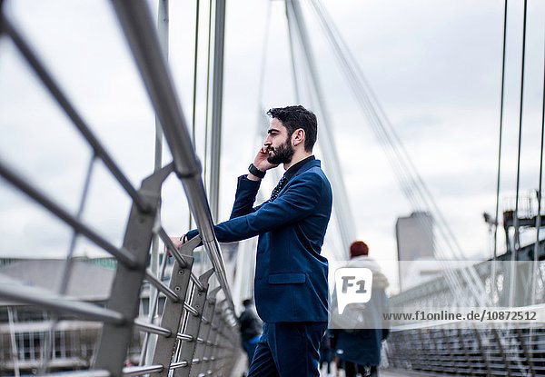 Geschäftsmann steht auf der Fußgängerbrücke und spricht über Smartphone  London  UK
