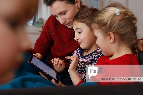 Mutter und Töchter auf dem Sofa sitzend mit digitalem Tablet lächelnd