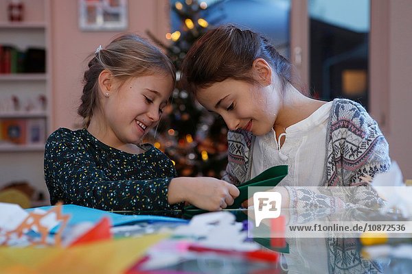 Mädchen bei Tisch beim Basteln von Weihnachtszeitungen lächelnd